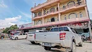 A multi-story building with a pink facade, a signboard with "WISMA 35" and "NOTARIS & PPAT" visible, and a parking area with several white pickup trucks.