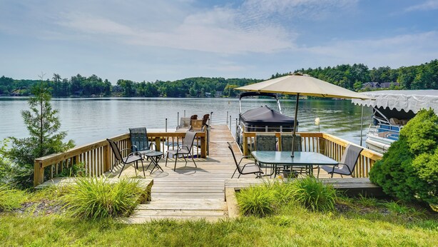 A wooden deck with outdoor furniture overlooking a lake, a covered seating area, and a boat docked nearby. - 1902 Family Lakehouse: Screened Porch & Views (Queensbury)