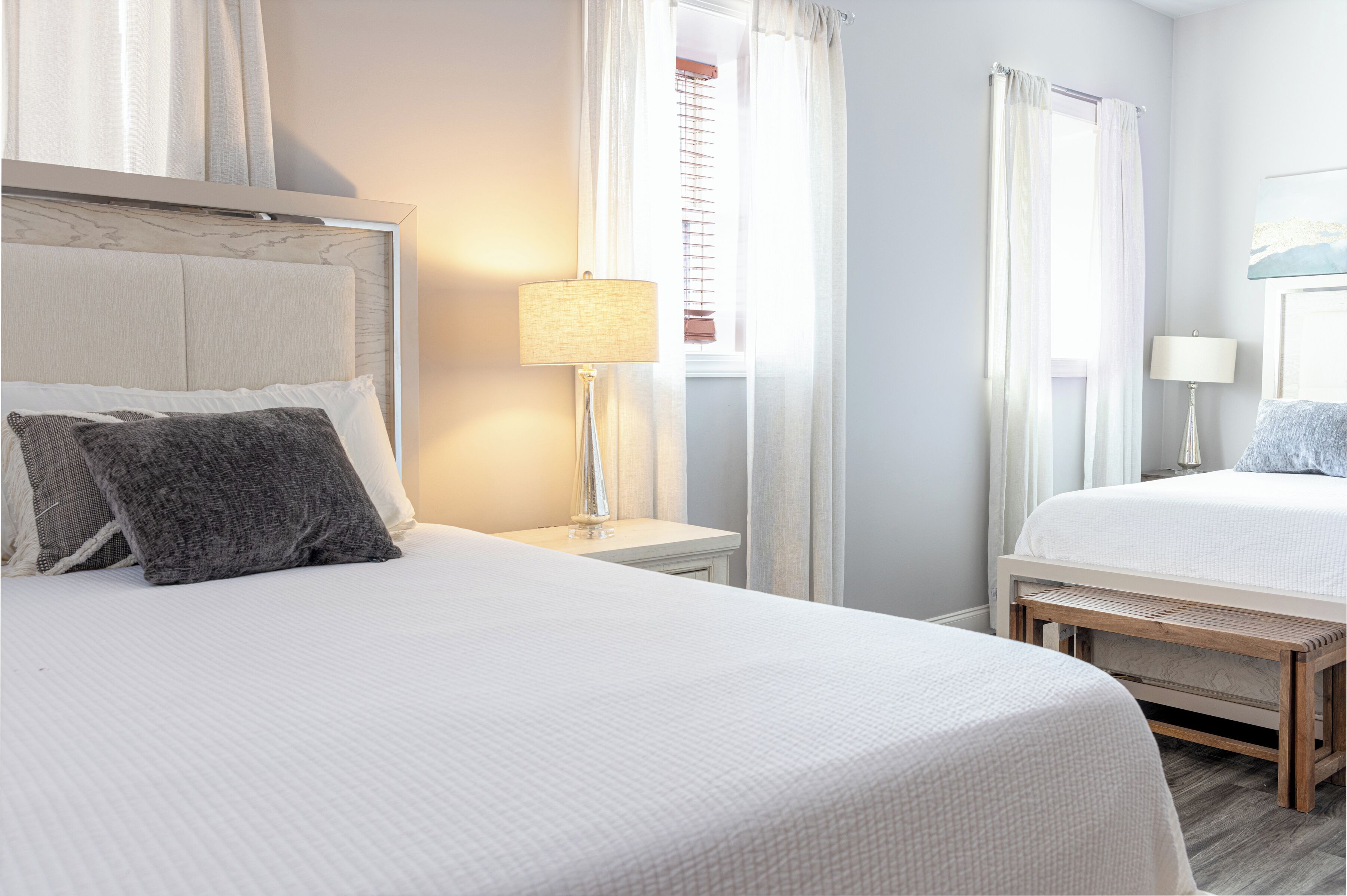Une chambre d’hôtel avec deux lits, une table de chevet avec une lampe et une fenêtre avec des rideaux.