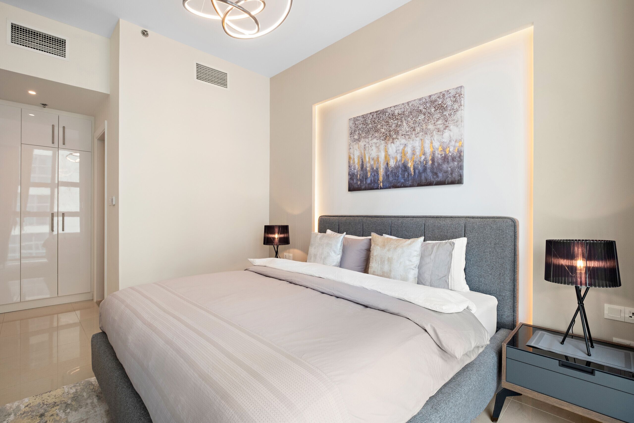 A modern bedroom with a large bed, bedside tables, a wall-mounted artwork, and a wardrobe.