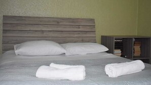 A neatly made bed with white linens and pillows, a wooden headboard, and a small bookshelf with books. - Veranda Vere (Tbilisi)