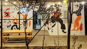 An outdoor area with a wooden bench, a potted plant, and a wall with colorful murals. - Veranda Vere (Tbilisi)
