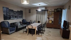 A living room with a sofa, dining table, chairs, a TV, and a cabinet with framed pictures. - Veranda Vere (Tbilisi)