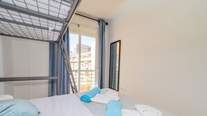 A hotel room with a bunk bed, a large window with curtains, a mirror, and neatly folded towels.