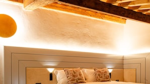 Quarto com teto de madeira, uma cama com cabeceira, mesas de cabeceira e um criado-mudo.