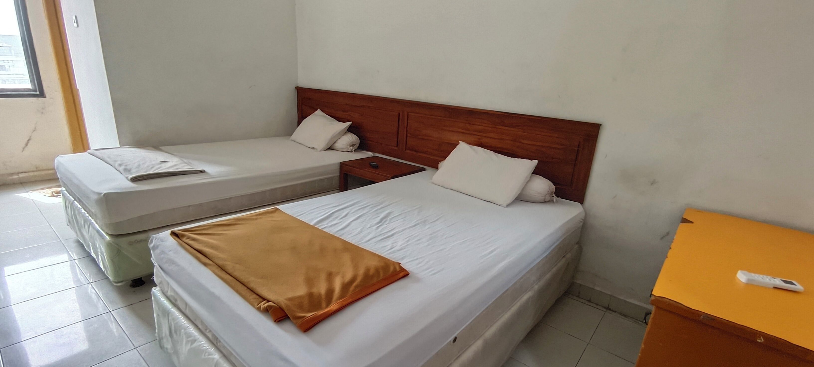 Two single beds with wooden headboards, a small bedside table, and a nightstand with a remote control.