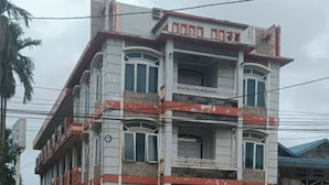 A multi-story building with a balcony on the second floor, a gated entrance, and a parked car in front.