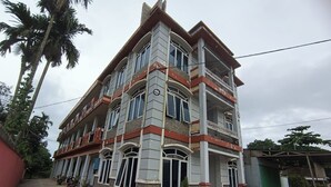 A multi-story building with a balcony on the second floor, a red and grey facade, and a concrete ground floor.
