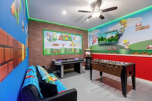 A room with a foosball table, a sofa, and a ceiling fan.