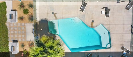 An aerial view of a swimming pool area with a tiled deck, lounge chairs, and potted plants.