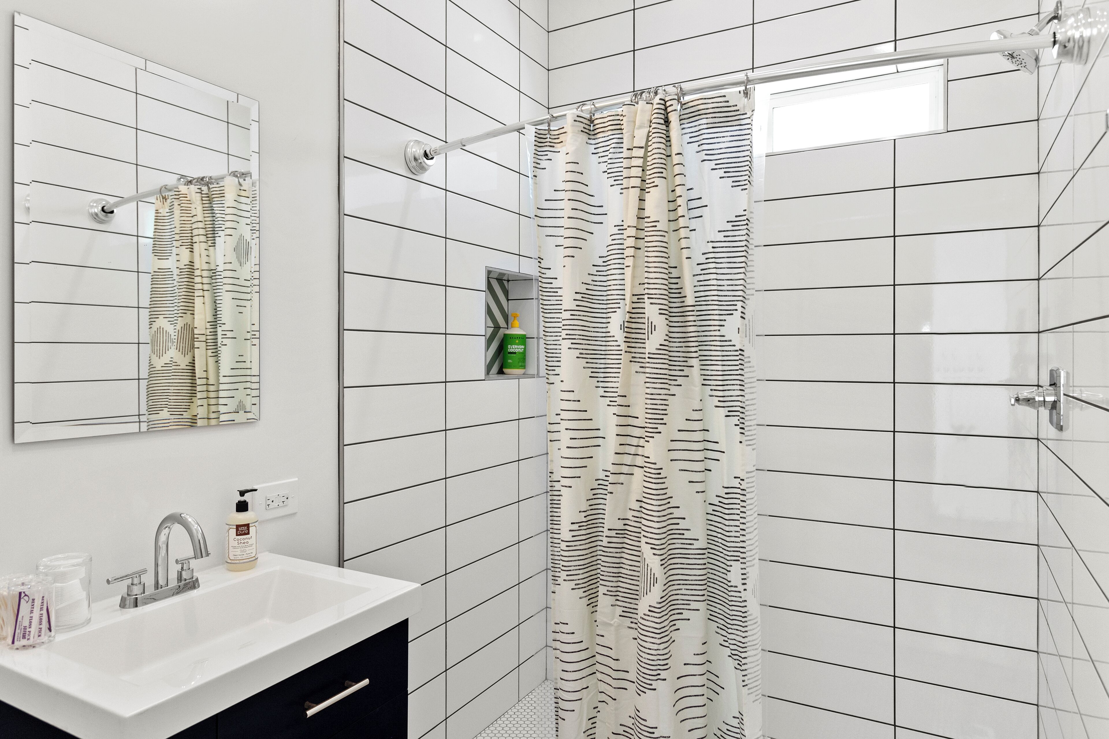 A modern bathroom with a white sink, mirror, and shower curtain with a geometric pattern.