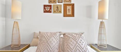 A bedroom with a bed, two bedside tables, a lamp on each table, and six framed artworks on the wall.