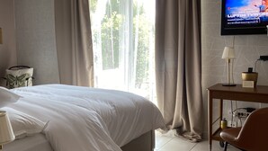 Habitación de hotel con una cama grande, un escritorio con silla, televisor montado en la pared y una ventana con cortinas.