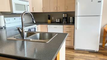 A modern kitchen with a stainless steel sink, a microwave, a refrigerator, and wooden cabinets.