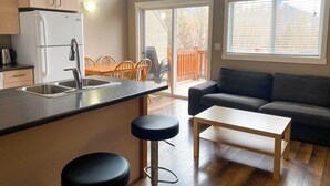 Eine kompakte Küche mit Kühlschrank, Spüle und Barhocker, ein Essbereich mit Stühlen und ein Sofa.