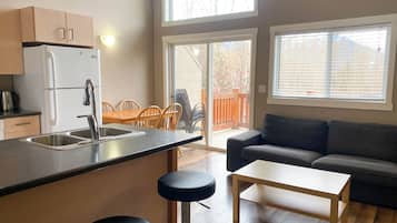 A compact kitchen with a refrigerator, sink, and bar stools, a dining area with chairs, and a sofa.