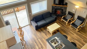 Ein modernes Wohnzimmer mit einer Couch, zwei Sesseln, einem Kamin, einem Deckenventilator und einer Küchenzeile mit Spüle.