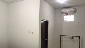 A room with a bed, a door, an air conditioning unit, and a small window.
