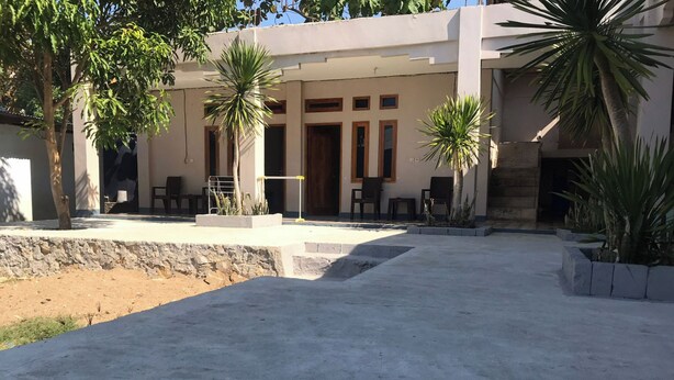 A building with a concrete patio, palm trees, and a stone wall.