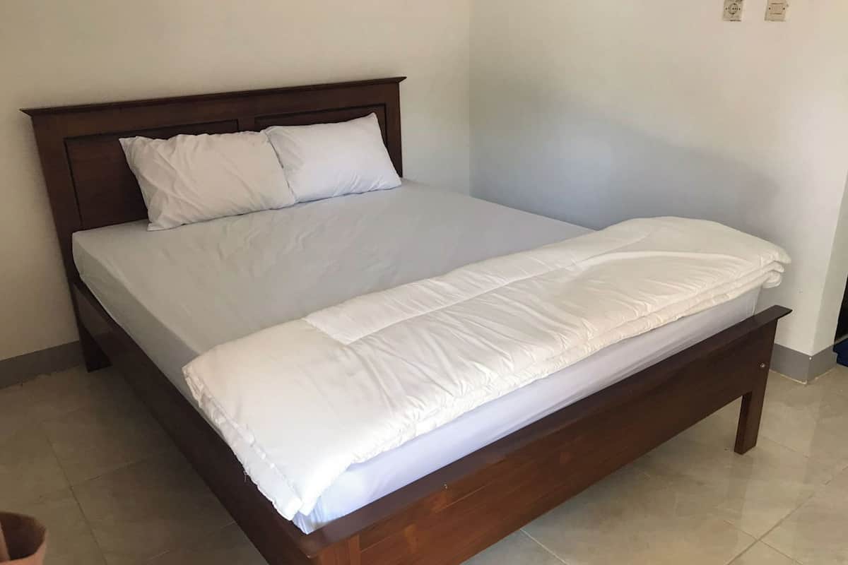 A single-bed room with a wooden headboard, white bedding, and a tiled floor.