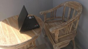 A laptop on a round wooden table and a rustic wooden chair.