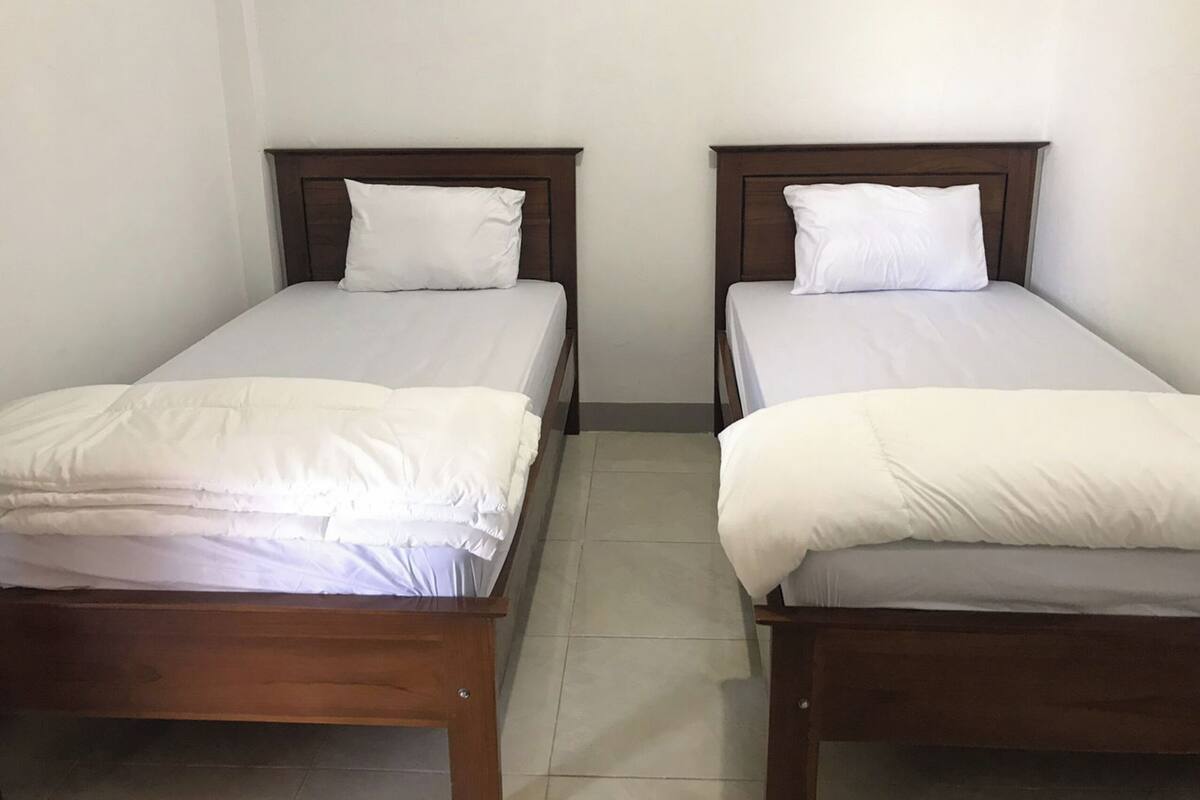 Two single beds with wooden headboards and white bedding in a room with plain walls and a tiled floor.