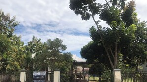 A gated entrance with a signboard, surrounded by trees and a clear sky.