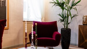 A room with a round table, a red sofa, a large potted plant, and a window with sheer curtains.