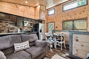 A cozy cabin interior with a kitchen, dining area, and a sofa with a 'be our guest' pillow.