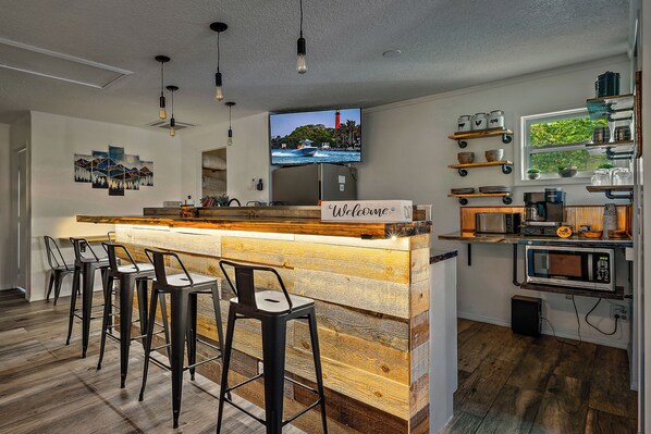 A modern kitchen with a bar area, wooden bar stools, a television, and various kitchen appliances.