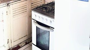 A kitchen with a gas stove, a white refrigerator, and a microwave on top. -  Sétimo Hostel 7 (São Paulo)