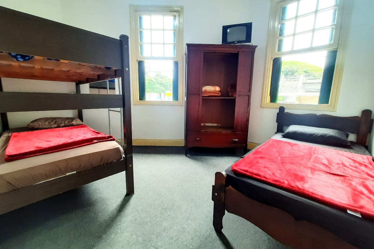 A room with two bunk beds, a wooden wardrobe, and a television on top.