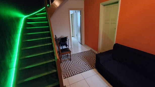 A staircase with green LED lighting, a black sofa, and a patterned rug in a room with orange walls. -  Sétimo Hostel 7 (São Paulo)