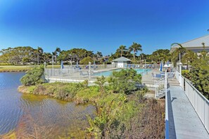 A pool area with a wooden deck, surrounded by palm trees and a body of water.