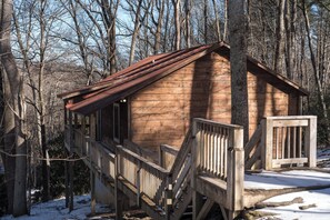 Eine Holzhütte mit einer Holztreppe, die zu einer Terrasse führt, umgeben von Bäumen und Schnee.
