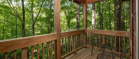 A wooden deck with metal chairs and a railing, surrounded by a forest.