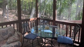 A covered outdoor area with a glass table and chairs, surrounded by wooden railings and a forest view. - Cozy Fall retreat in Massanutten Four Season Mountain Resort ski, bike, fish (McGaheysville)