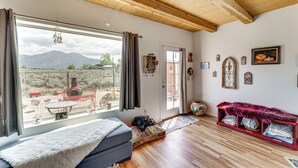 A room with a large window, wooden ceiling beams, a sofa, a red bench, and various wall decorations. - Pet-Friendly El Prado Vacation Rental w/ Views! (El Prado)