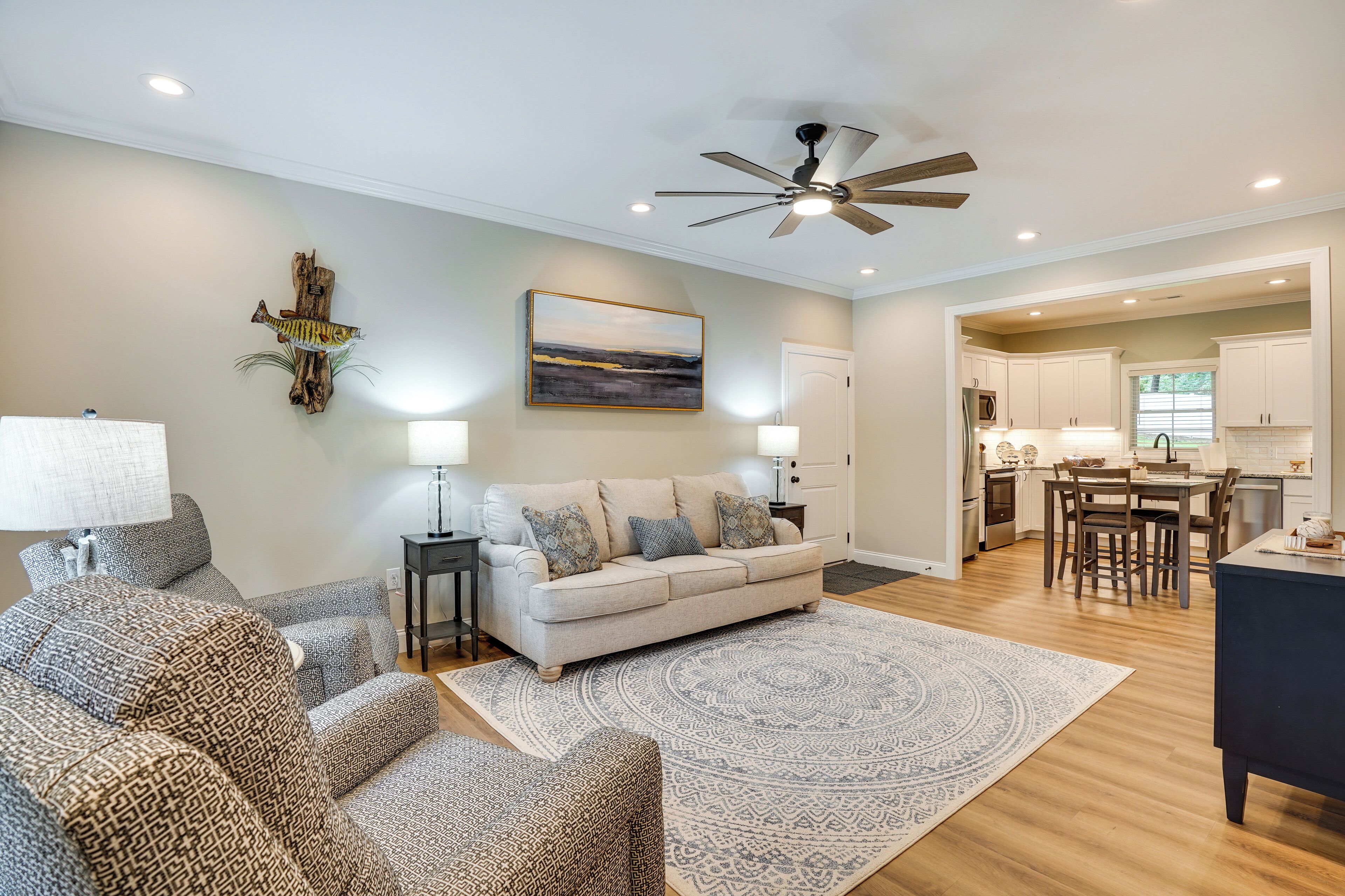 A living room with a sofa, patterned chairs, a coffee table, a rug, a ceiling fan, and a painting on the wall.
