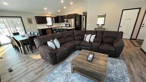 A modern living room with a sectional sofa, a dining table, and a kitchen in the background. - The Ridge - NEW Modern Home! (Onamia)