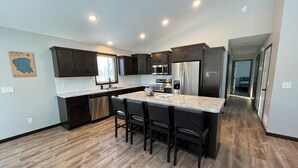 A modern kitchen with dark wood cabinets, a stainless steel refrigerator, a built-in oven, and a granite countertop island with bar stools. - The Ridge - NEW Modern Home! (Onamia)