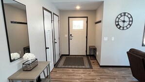 A modern interior with a wooden floor, a central door, a clock on the wall, and a small table with a vase. - The Ridge - NEW Modern Home! (Onamia)