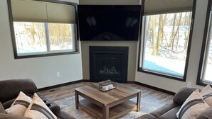 A living room with a fireplace, a flat-screen TV, and a large window. - The Ridge - NEW Modern Home! (Onamia)