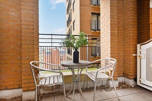 A small outdoor balcony with a round table and two chairs, a potted plant, and a view of a brick building in the background. - London Choice -South Kensington-Museums (London)