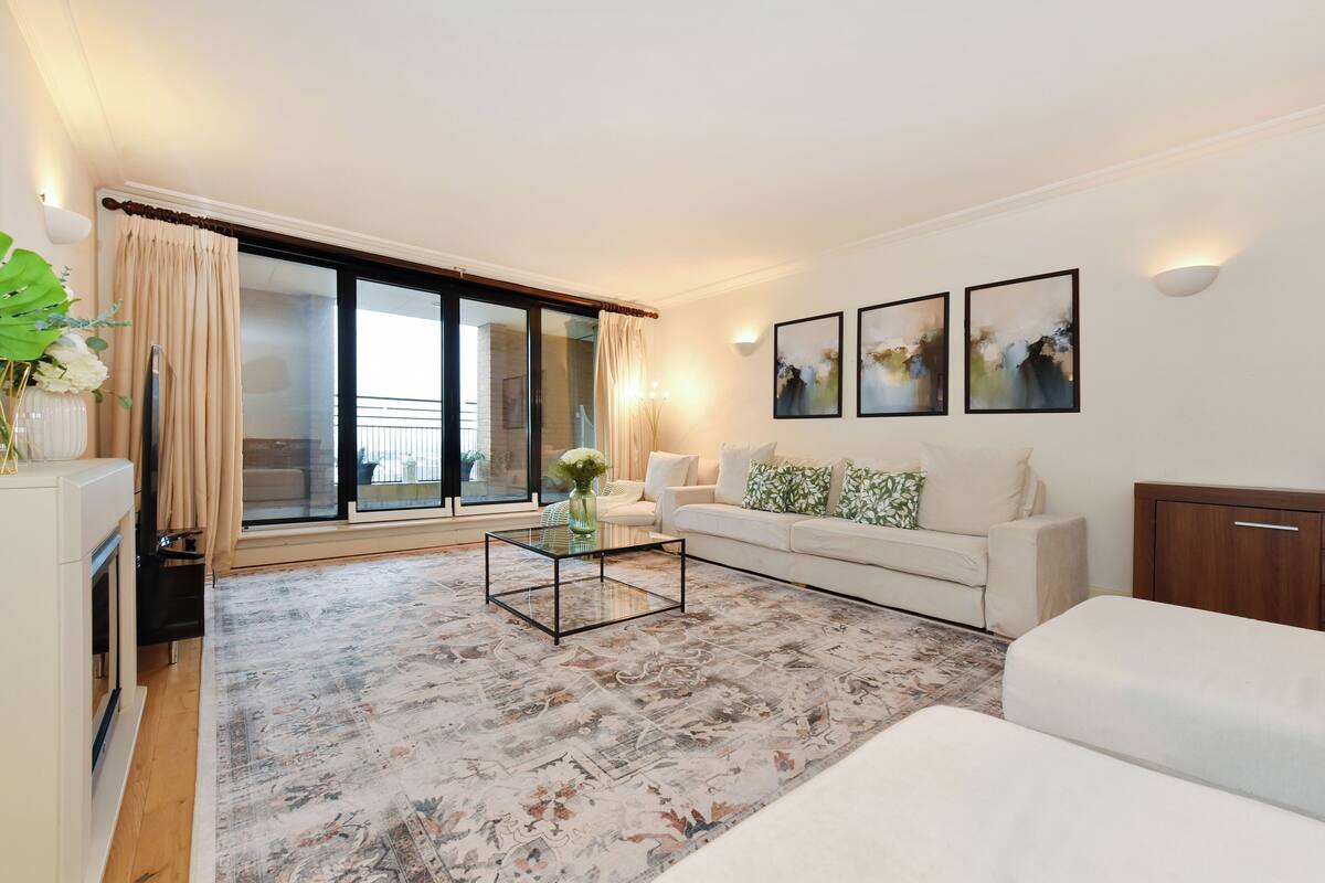 Ein modernes Wohnzimmer mit einer Couch, einem Couchtisch und einem großen Fenster mit Vorhängen.