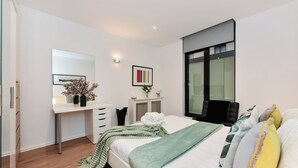A modern bedroom with a bed, bedside table, dresser, and a large mirror. - London Choice -South Kensington-Museums (London)