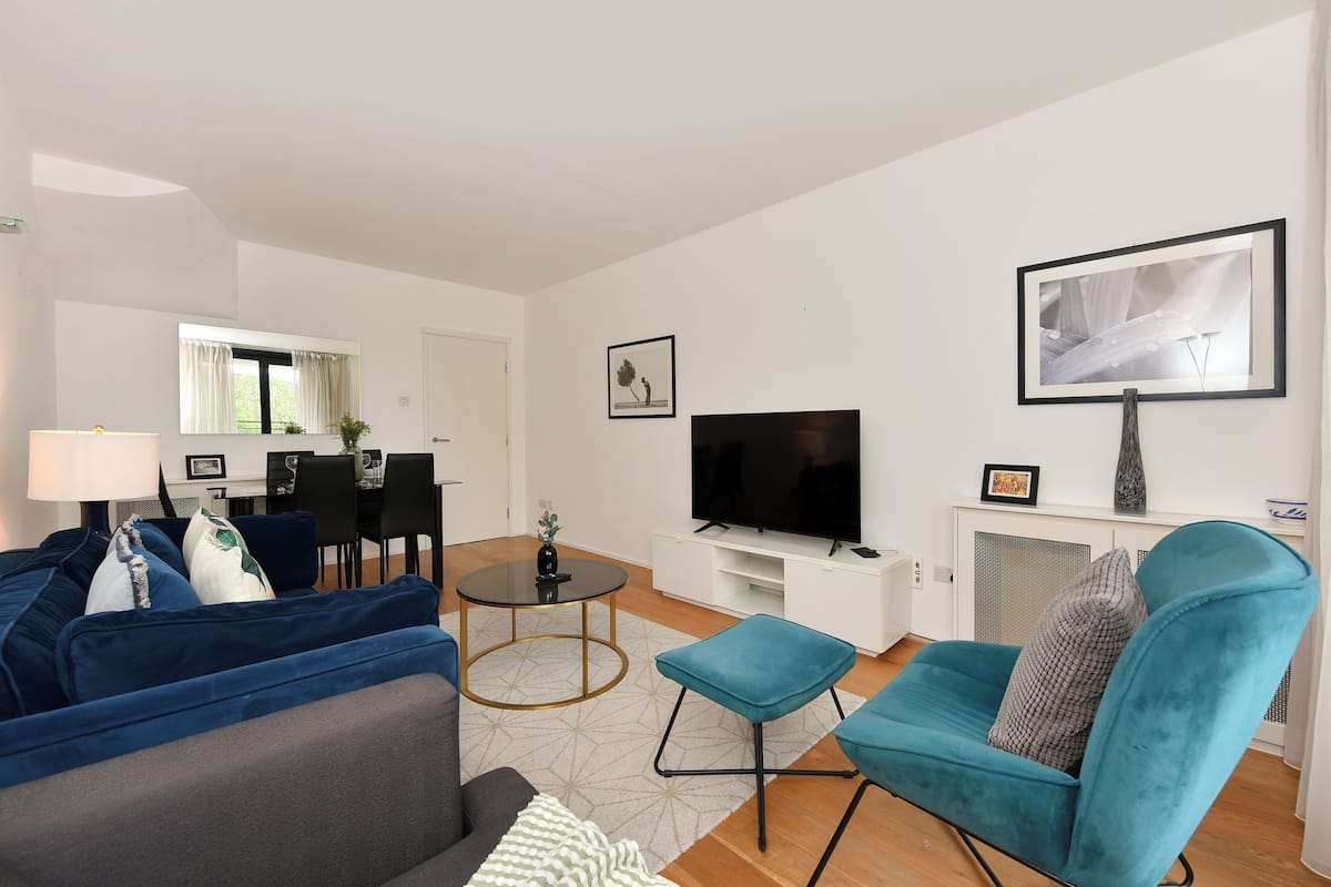 Ein modernes Wohnzimmer mit einer Couch, Hocker, Fernseher und Kunstwerken an der Wand.