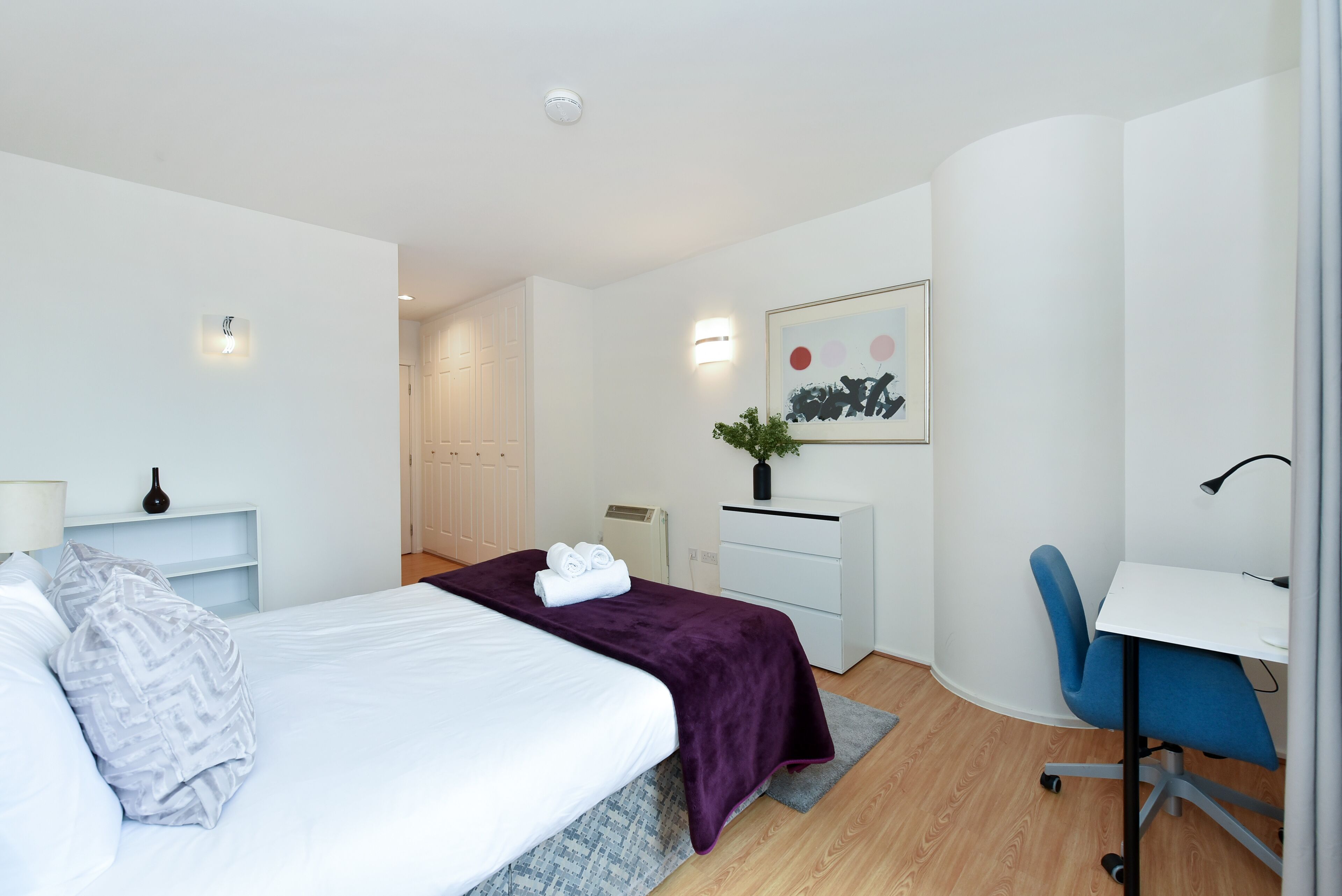 A modern hotel room with a bed, desk, chair, and a small plant.