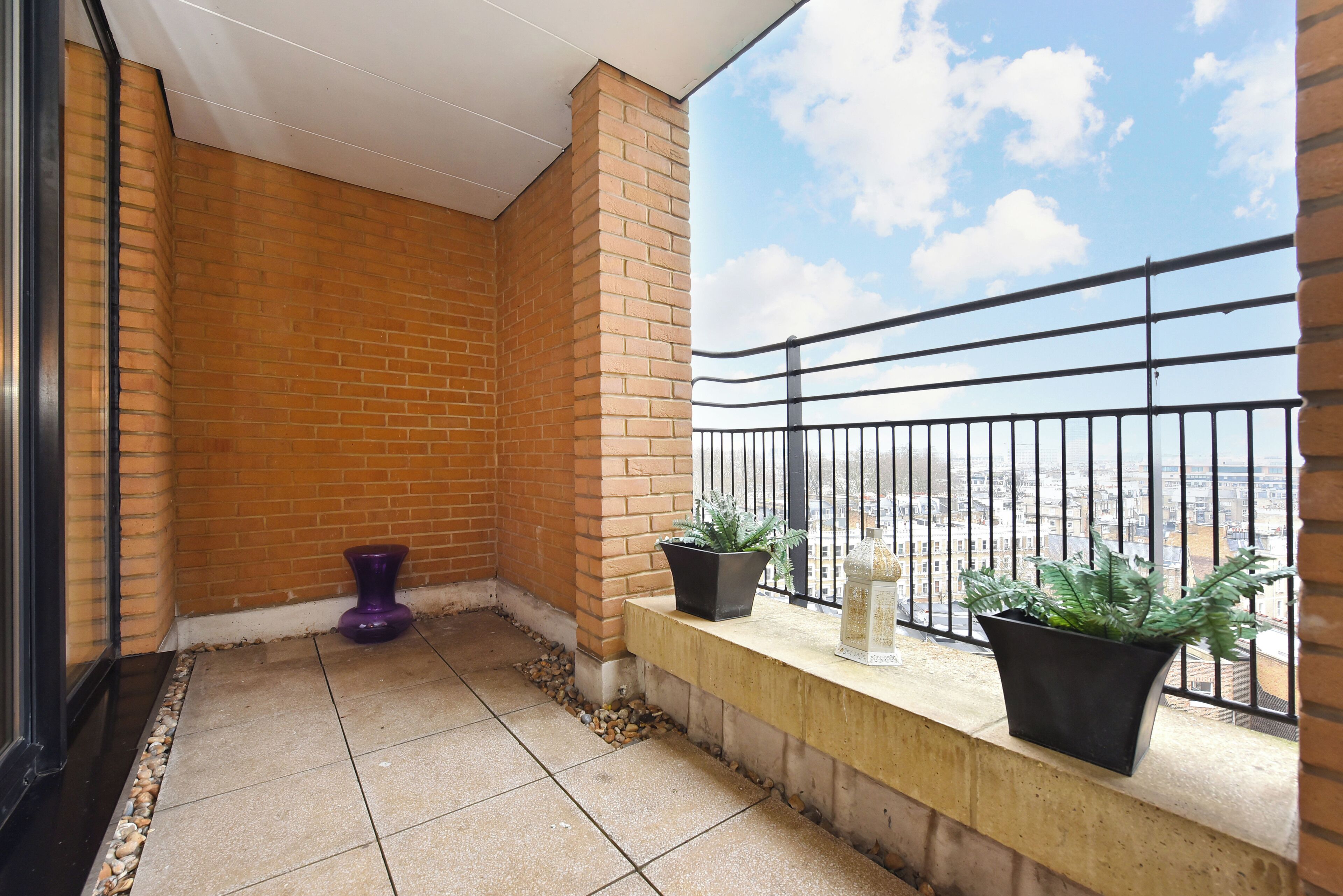 A balcony with a brick wall, two potted plants, and a view of the cityscape.