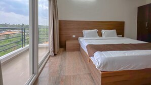 Habitación de hotel con un ventanal grande, cabecera de madera, dos camas y vistas a un estacionamiento y zonas verdes.